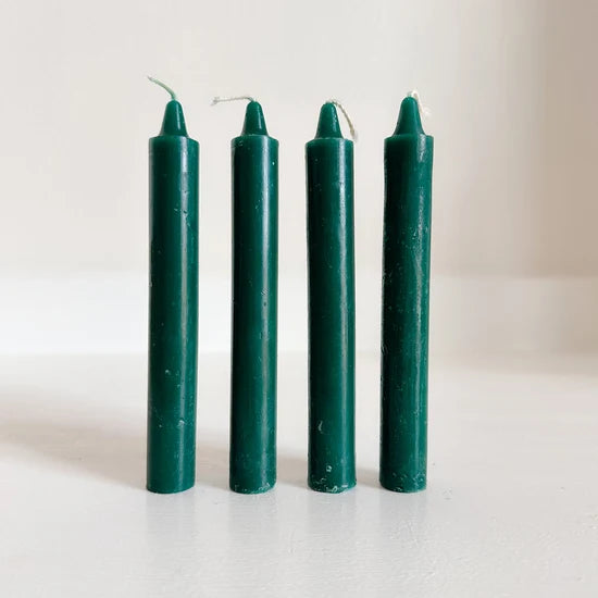 Four dark green altar candles standing upright on a plain white surface against a light neutral background.