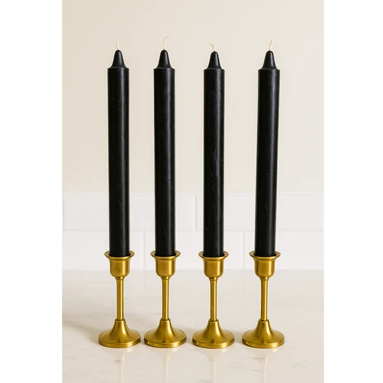 Four black altar candles in matching gold candlesticks, arranged side by side on a light marble surface against a white tiled wall.