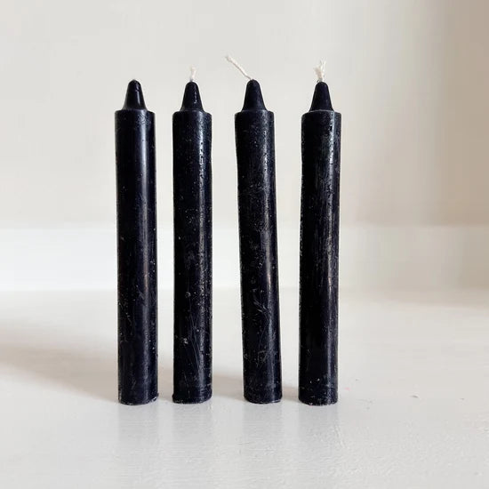 Four black altar candles with white wicks standing upright on a light surface against a plain light background.