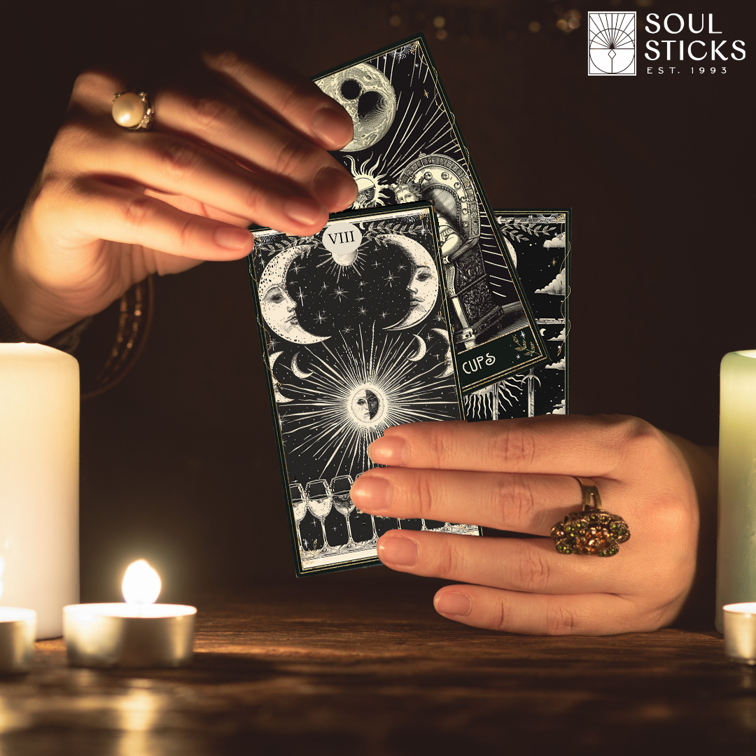 Cards held by candlelight:
“Hands holding The Mystic’s Path tarot cards by candlelight, with moon faces and sunburst artwork.”