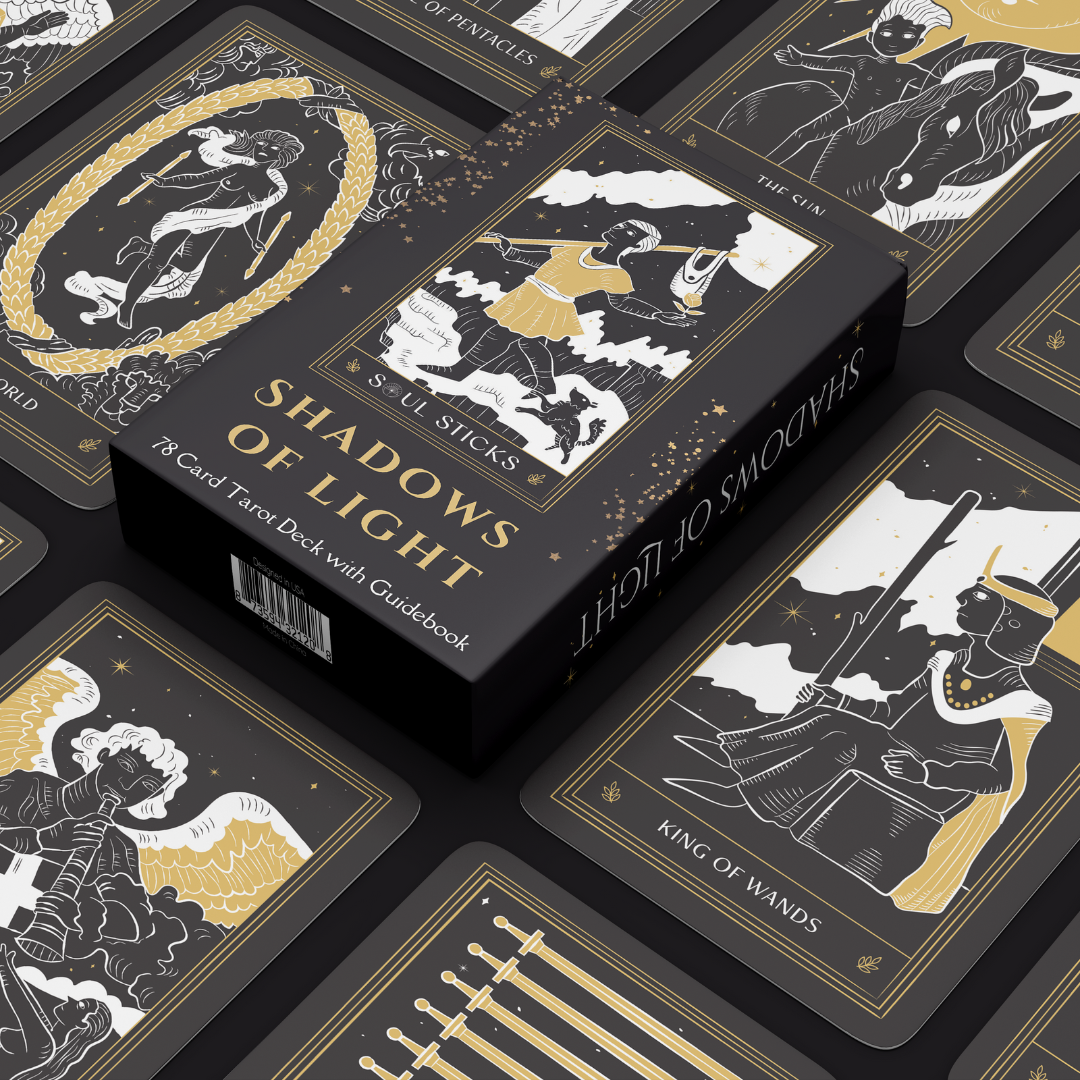 Box surrounded by cards: “Shadows of Light tarot box surrounded by black, white and gold cards, including The World and King of Wands.”
