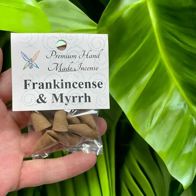 Crystal Fairy Patch Frankincense and Myrrh hand-made cone incense in a clear plastic bag held against a green leaf background.