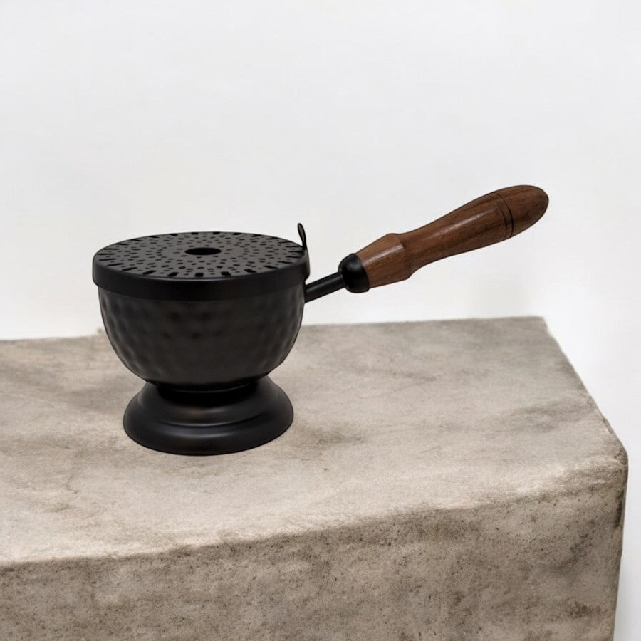 Crystal Fairy Patch 9-inch matte black hammered iron cauldron incense burner with a perforated lid and wooden handle on stone.