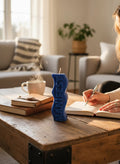 Crystal Fairy Patch handcrafted blue sculptural candle with MANIFEST lettering on a wooden table with a person writing in a journal