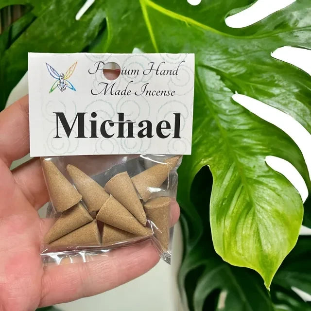 Crystal Fairy Patch Michael premium hand-made cone incense in a clear plastic bag held against a large green monstera leaf.