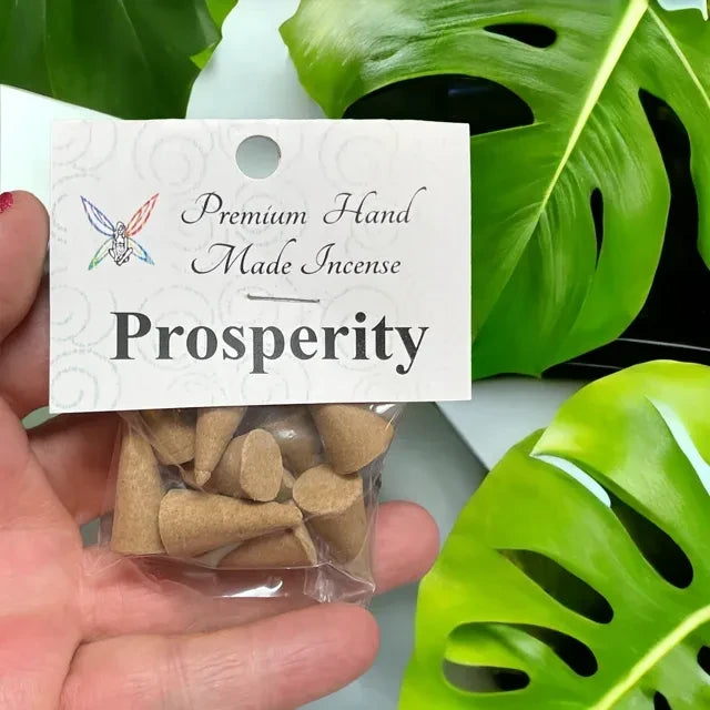 Crystal Fairy Patch Prosperity premium hand made cone incense in a clear bag held against a monstera leaf background.