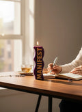 Crystal Fairy Patch purple wavy pillar candle with gold MANIFEST text, lit on a desk next to a person writing in a journal.