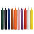 Nine colorful taper candles in green, black, blue, orange, pink, purple, red, white, and yellow, arranged in a row against a plain white background.