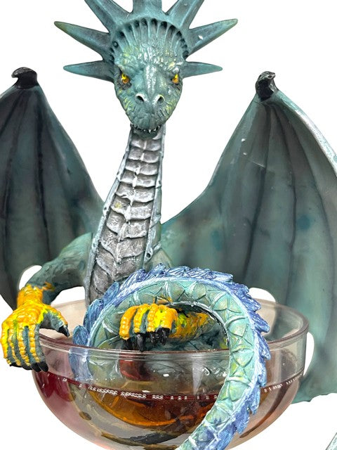 My Store "Manhattan" dragon figurine in teal and blue with yellow claws, resting in a glass of amber liquid.