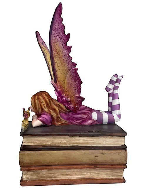 My Store Book Club Fae figurine of a fairy with purple wings, lying on stacked books, wearing striped socks.
